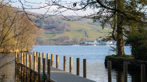 A jetty leading into a lake framed by autumn trees with mountains beyond